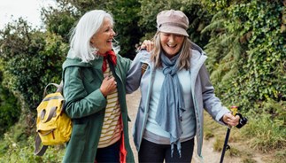 Female friends on a hike on a coastal path, laughing while they have their arms around each other.