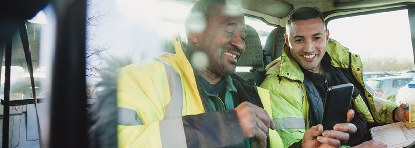 Two male employees sat in a van looking at a smartphone 
