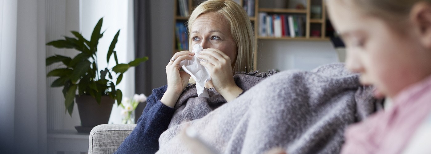 Woman with cold, flu or COVID symptoms on a sofa using a paper tissue