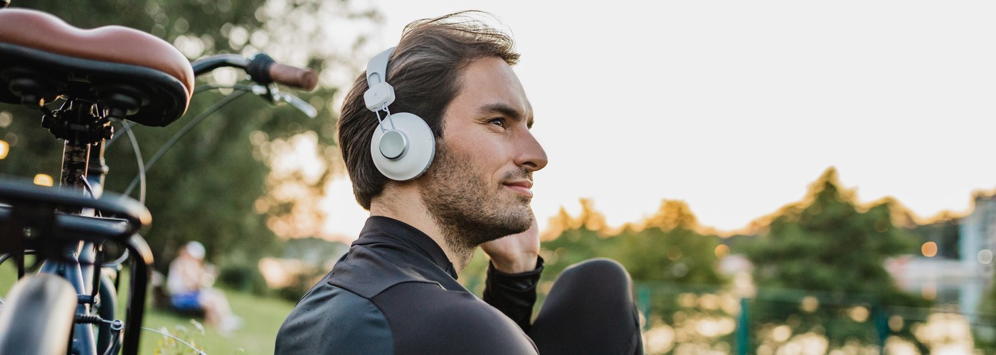 A young man sitting with his headphones on a park bench, with his bike next to him 