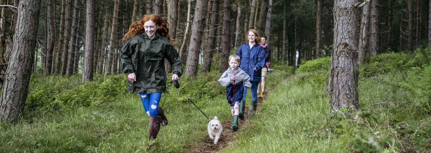 Teenage girl and dog leading family on hike through forest
